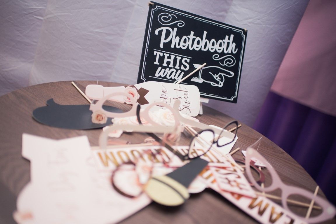 Photo booth prop table with oversized glasses, signs, and a chalkboard reading “Photobooth this way”