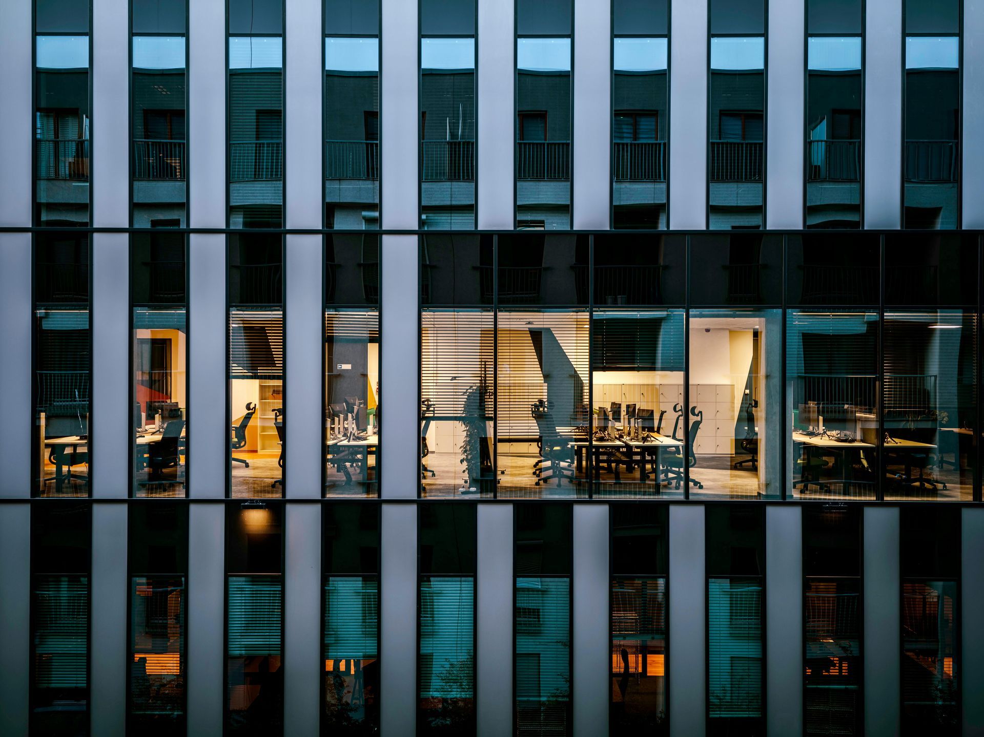 Office building facade at dusk, illuminated interiors reveal office workers.