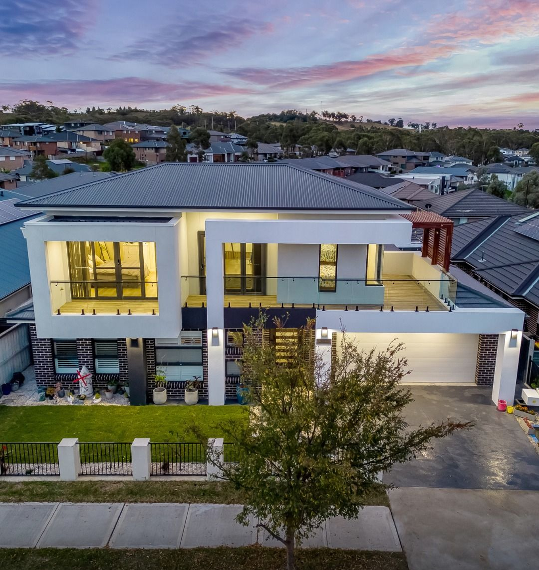 Modern two-story home at dusk with warm lit windows and a balcony, seen from the street — Matt Made Building in Camden, NSW