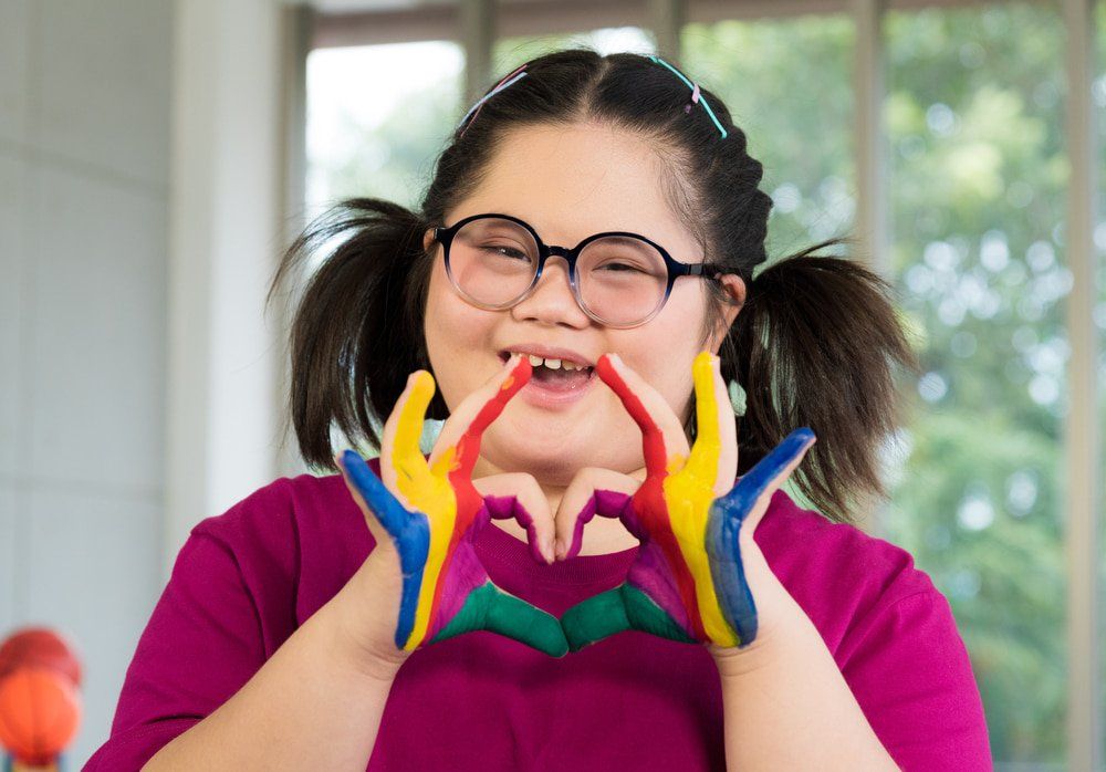 Girl With Down Syndrome With Colourful Painted Hands — NDIS Services in Yeppoon, QLD
