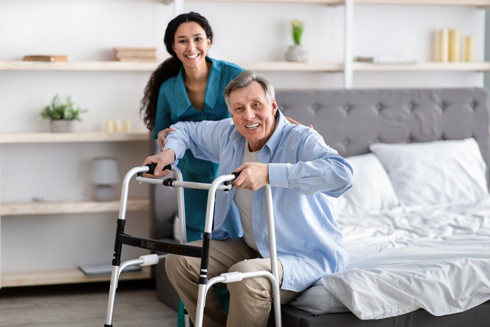 Woman Helping Elderly Man With Walking Frame To Stand Up From Bed — NDIS Services in Yeppoon, QLD