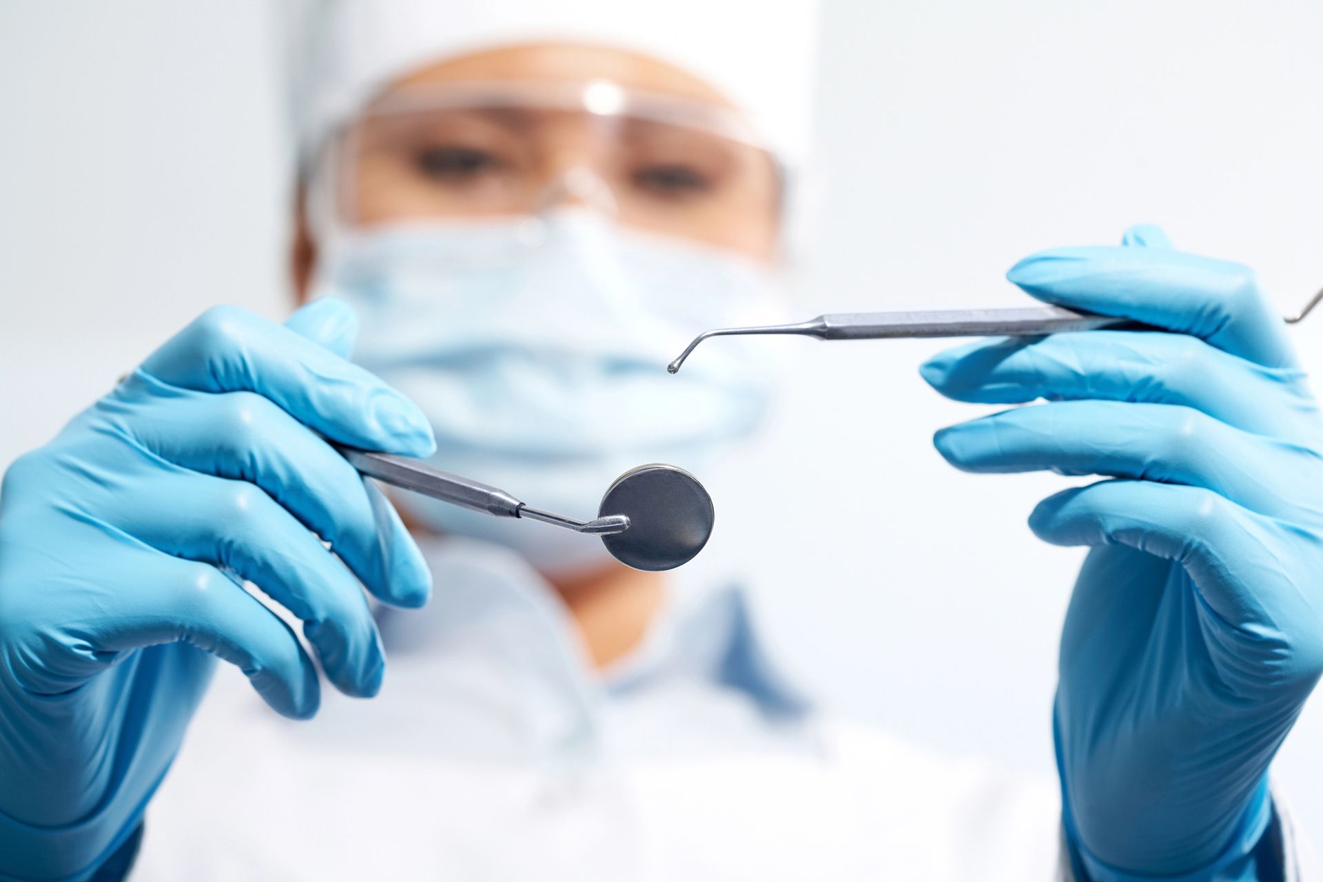 Dentista con guantes azules usando instrumental dental durante un procedimiento, con una máscara y gafas desenfoque al fondo.