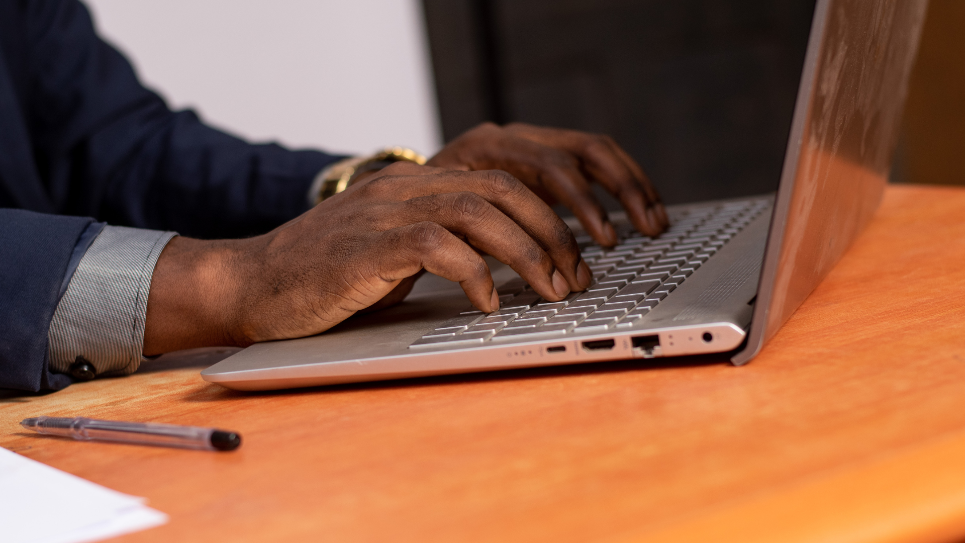 A man is typing on a laptop computer on a wooden desk.