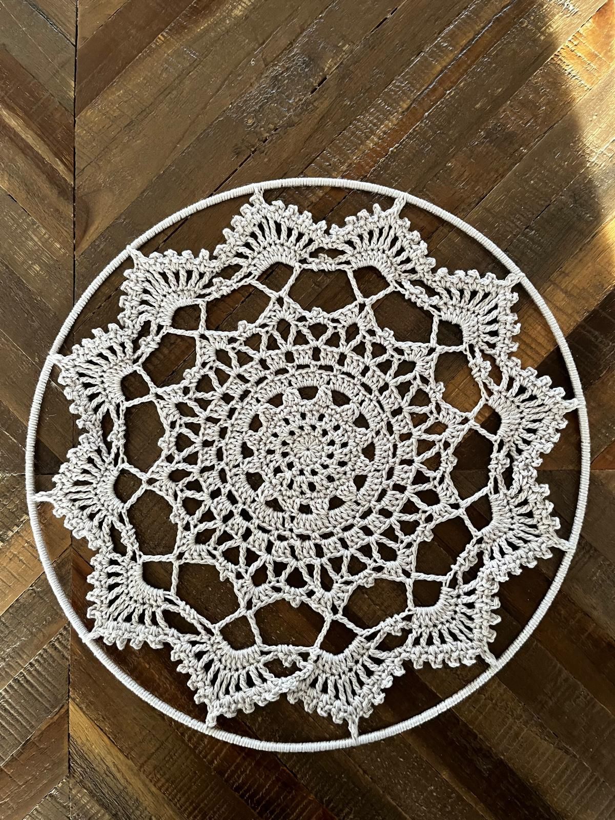 Een wit, gehaakt kleedje, rond en met een ingewikkeld kantpatroon, ligt op een houten ondergrond.