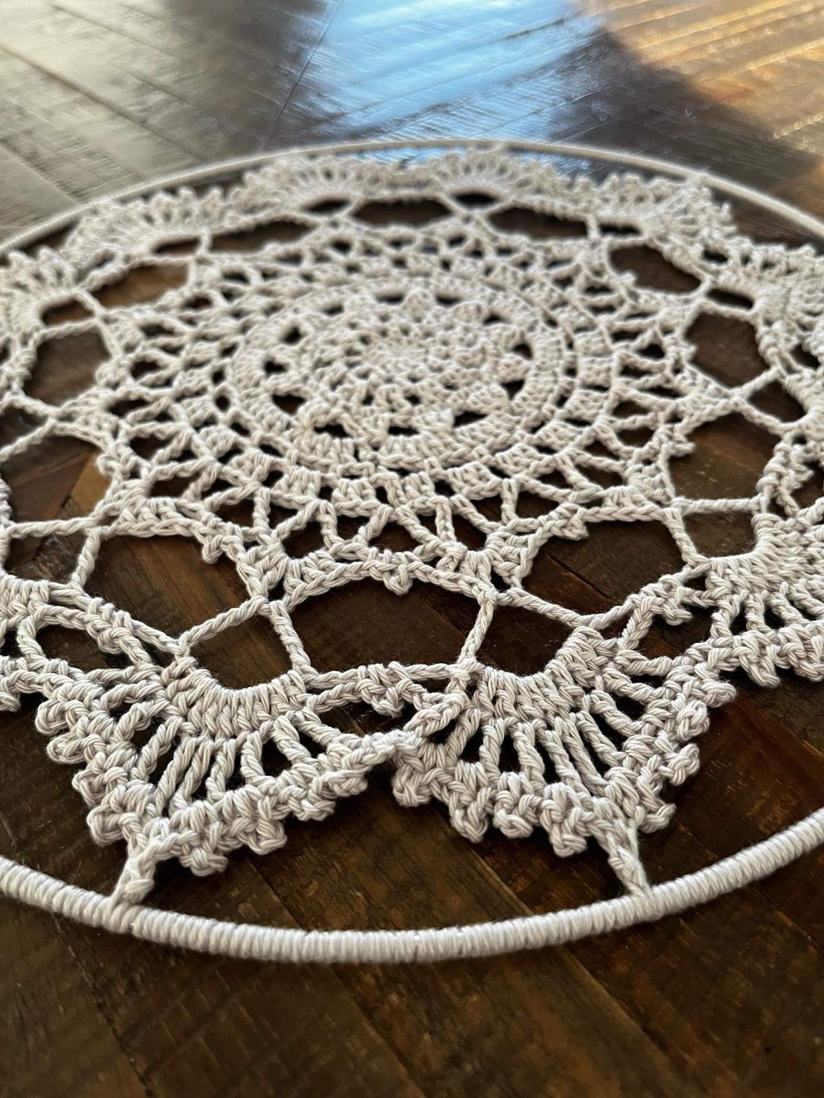 Een wit, gehaakt kleedje, rond en met een ingewikkeld kantpatroon, ligt op een houten ondergrond.