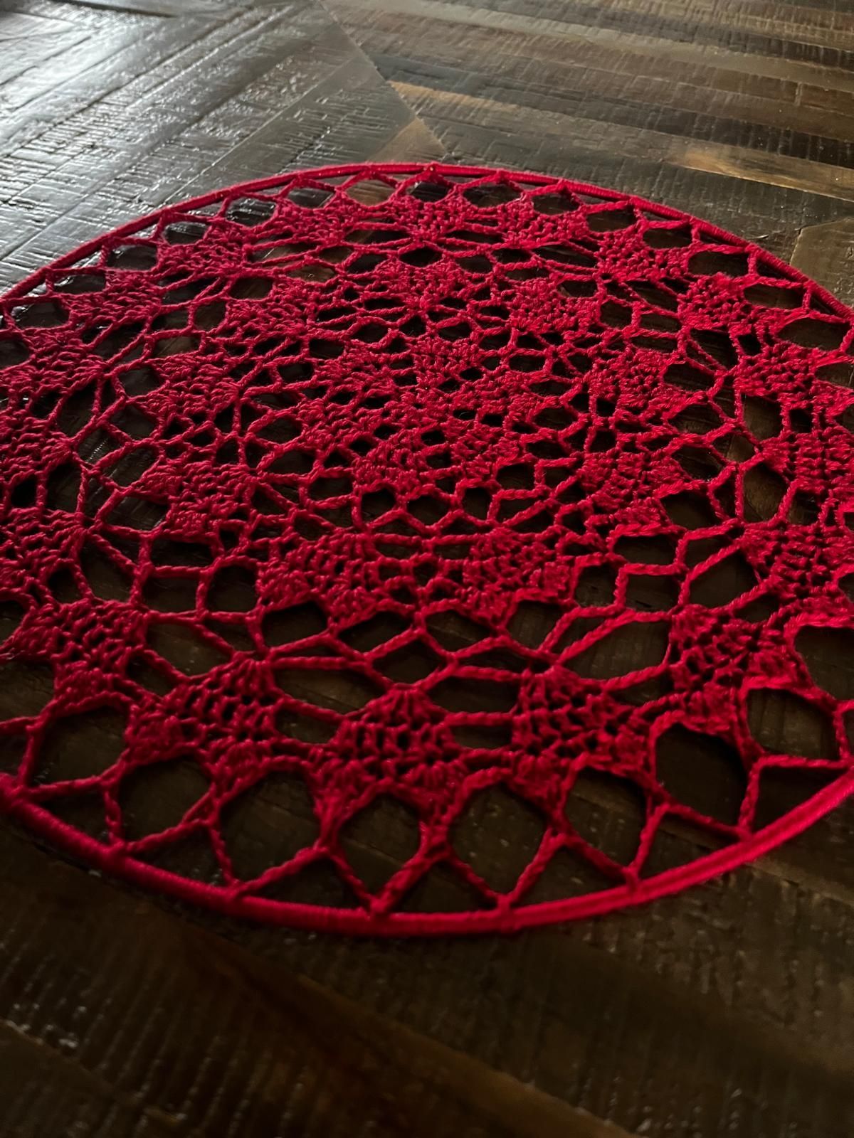 Een rood gehaakt kleedje met een ingewikkeld bloemenpatroon ligt op een donkere houten tafel.