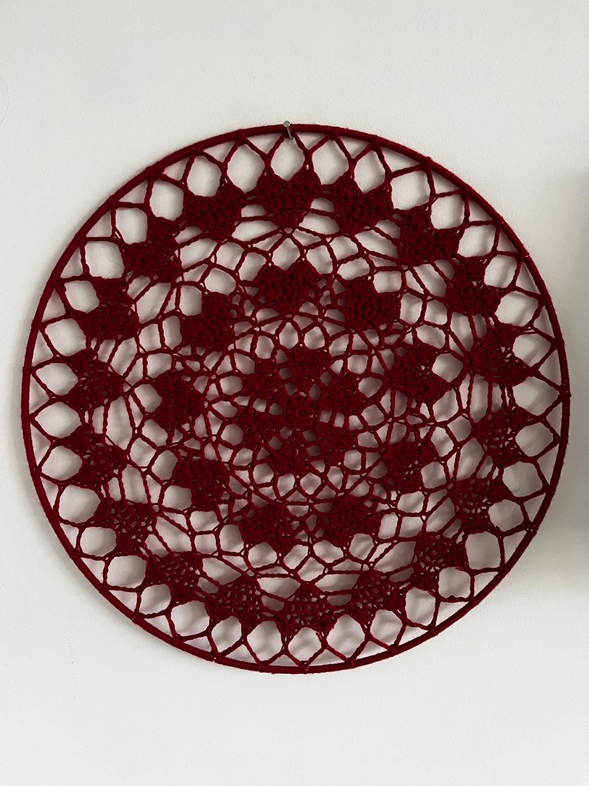 Een rood gehaakt kleedje met een ingewikkeld bloemenpatroon ligt op een donkere houten tafel.