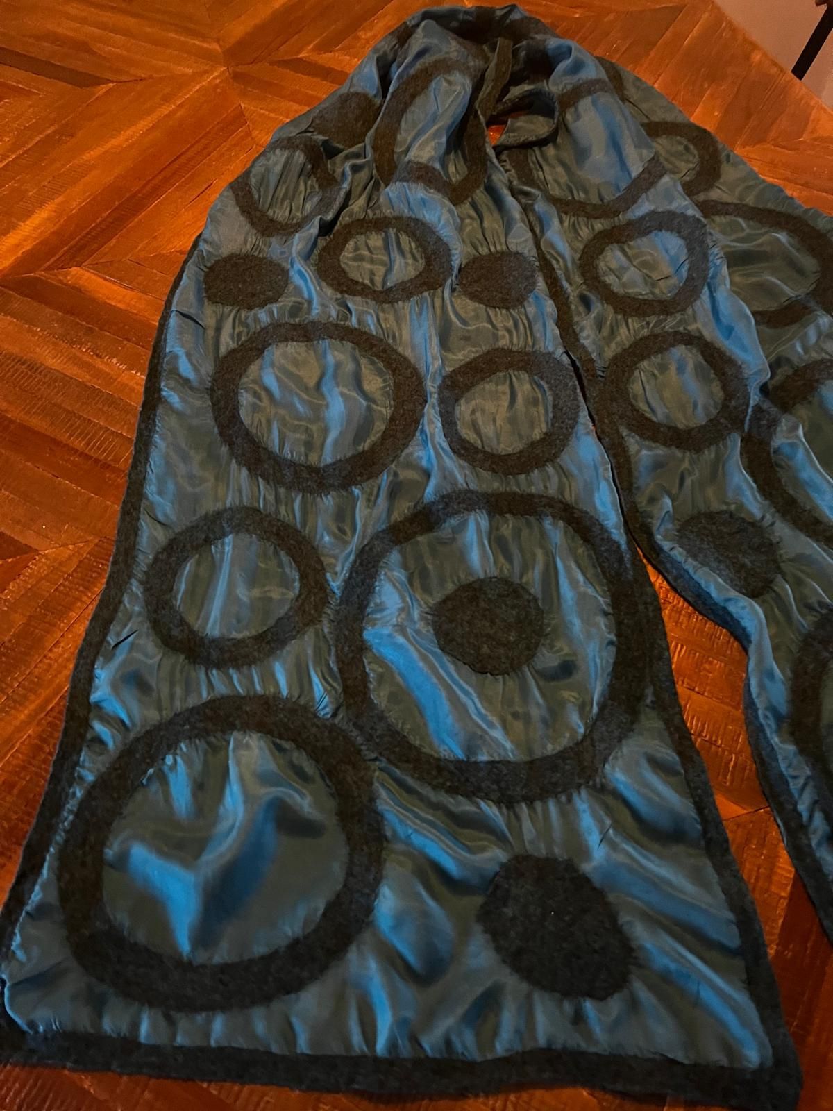 Een blauwe sjaal met zwarte cirkelvormige motieven ligt op een houten tafel.