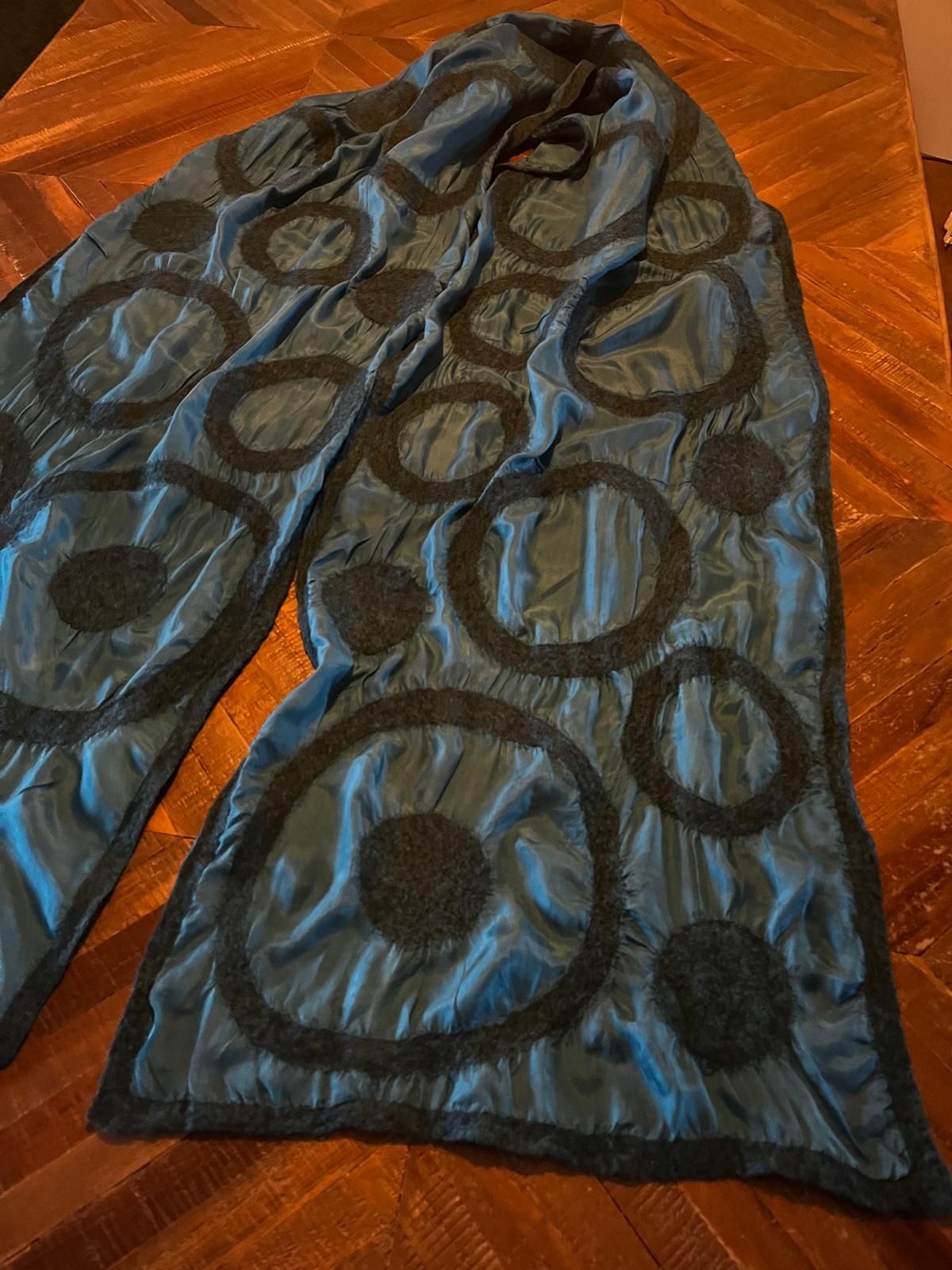 Een blauwe sjaal met zwarte cirkelvormige motieven ligt op een houten tafel.
