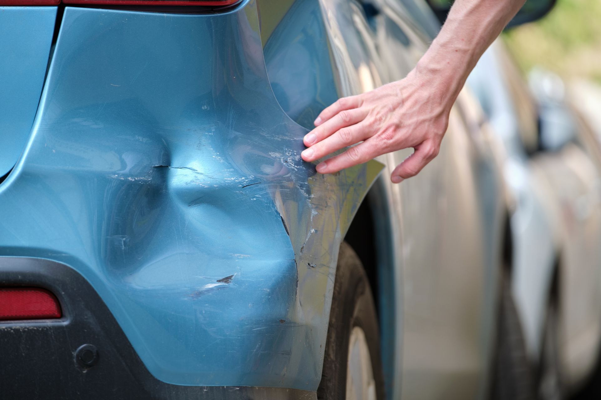 A person is touching a blue car with a damaged bumper.