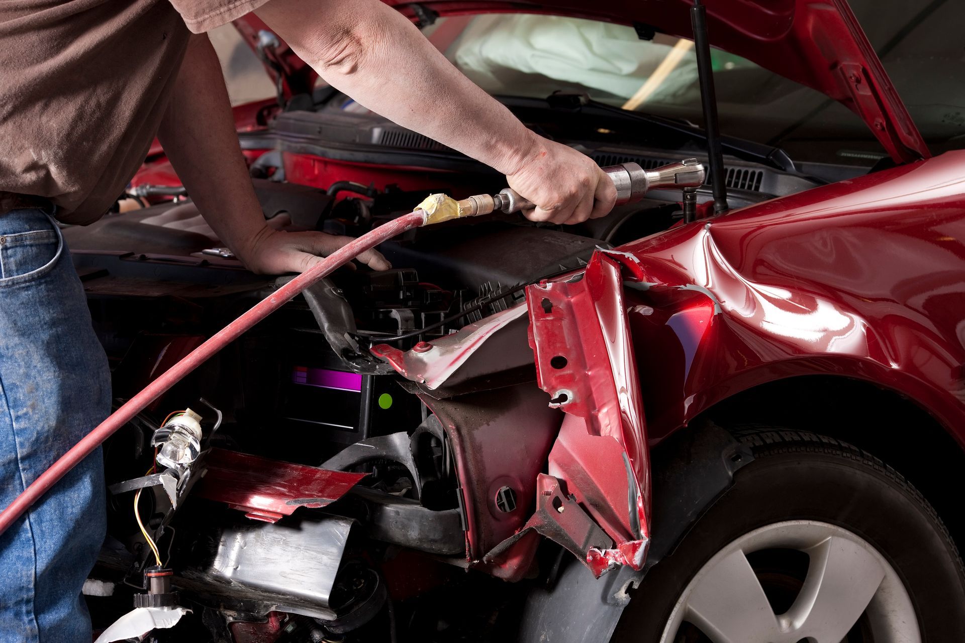 A man is working on a damaged red car with a hose.