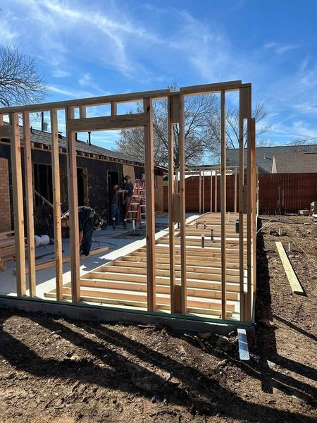 Wood-framed building under construction with workers, concrete foundation, and clear blue sky
