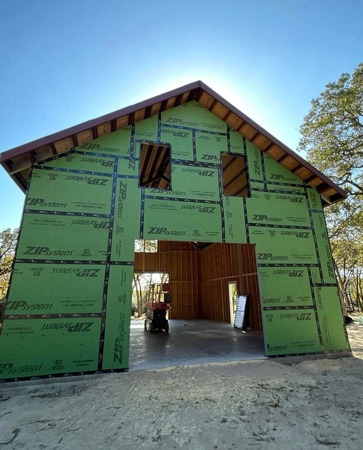 Green-sheathed barn under construction with open central passage and gabled roof