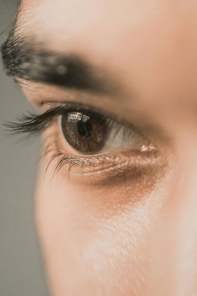 Close-up of brown eye, looking to the side. Visible eyebrow and eyelashes. Soft lighting.