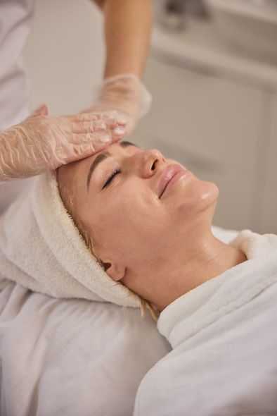 Woman receiving facial treatment; therapist's hands on her forehead, spa setting.