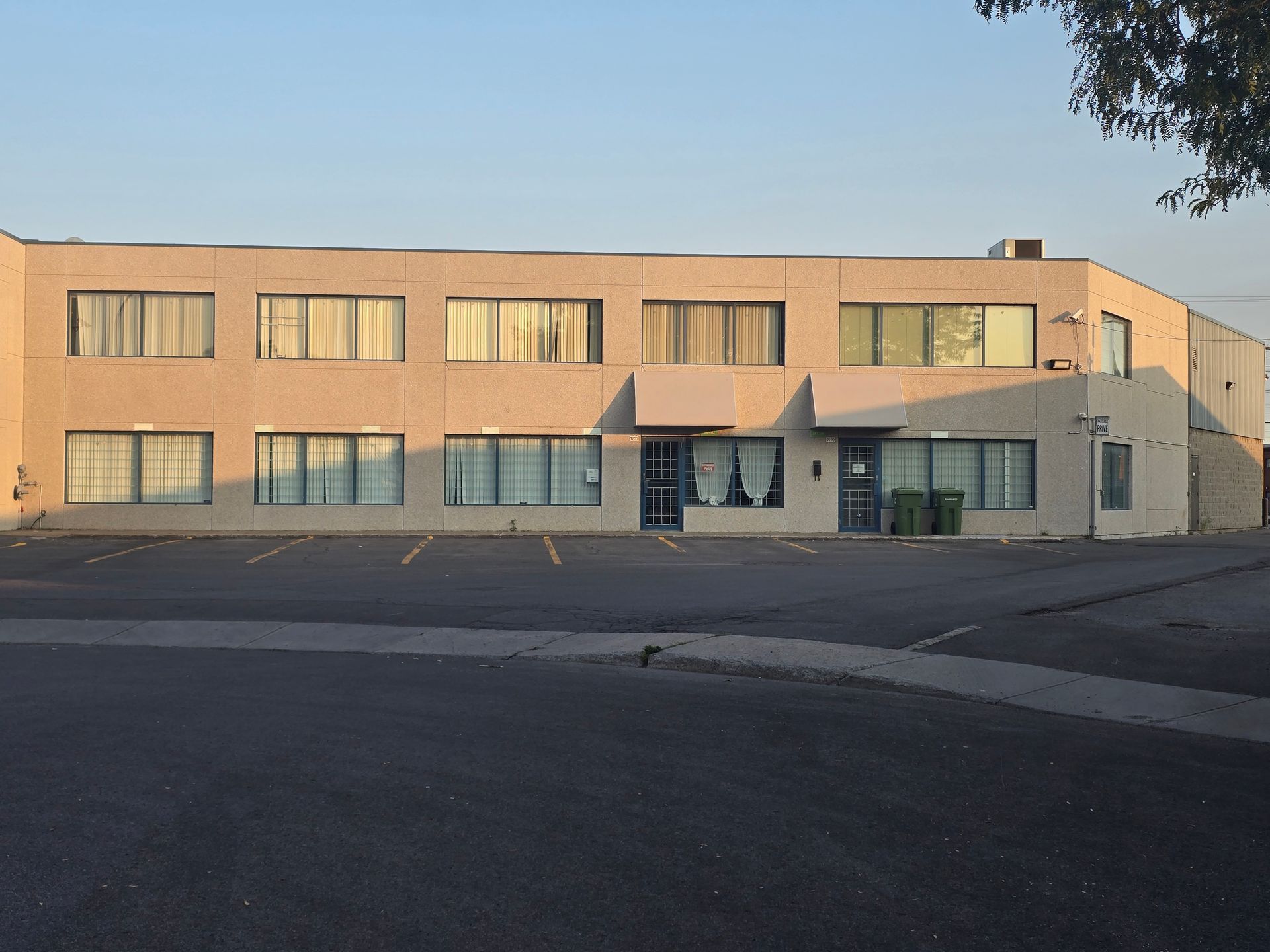 Two-story beige building with multiple windows and a parking lot in front under a clear sky.