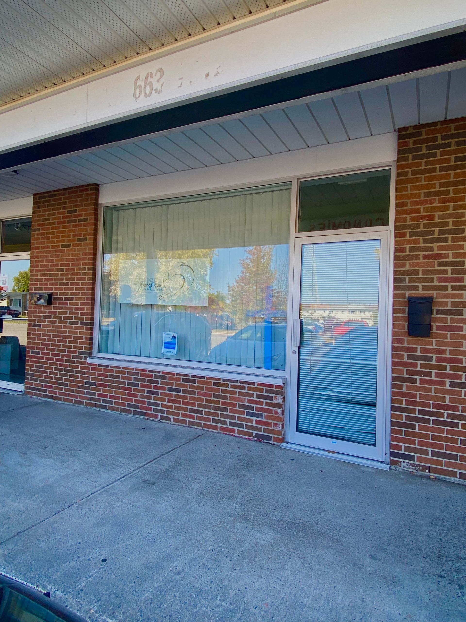 Exterior of a brick building with a glass door and large window. Number 663 is visible above the window.
