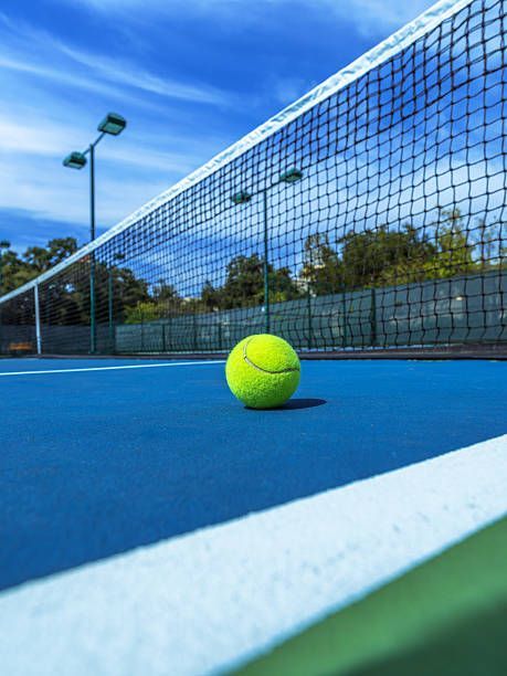 A tennis ball is sitting on a tennis court next to a net.