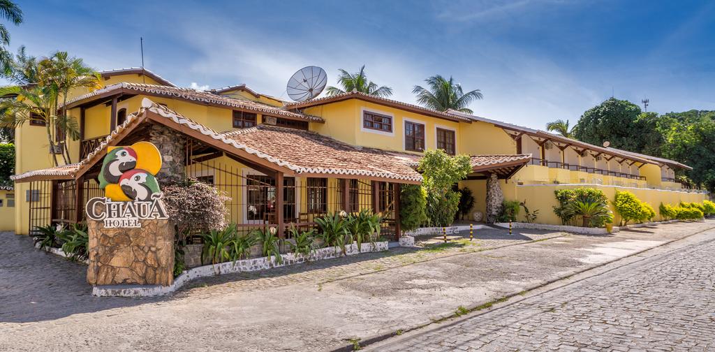 Uma grande casa amarela com telhado de tijolos é cercada por árvores.