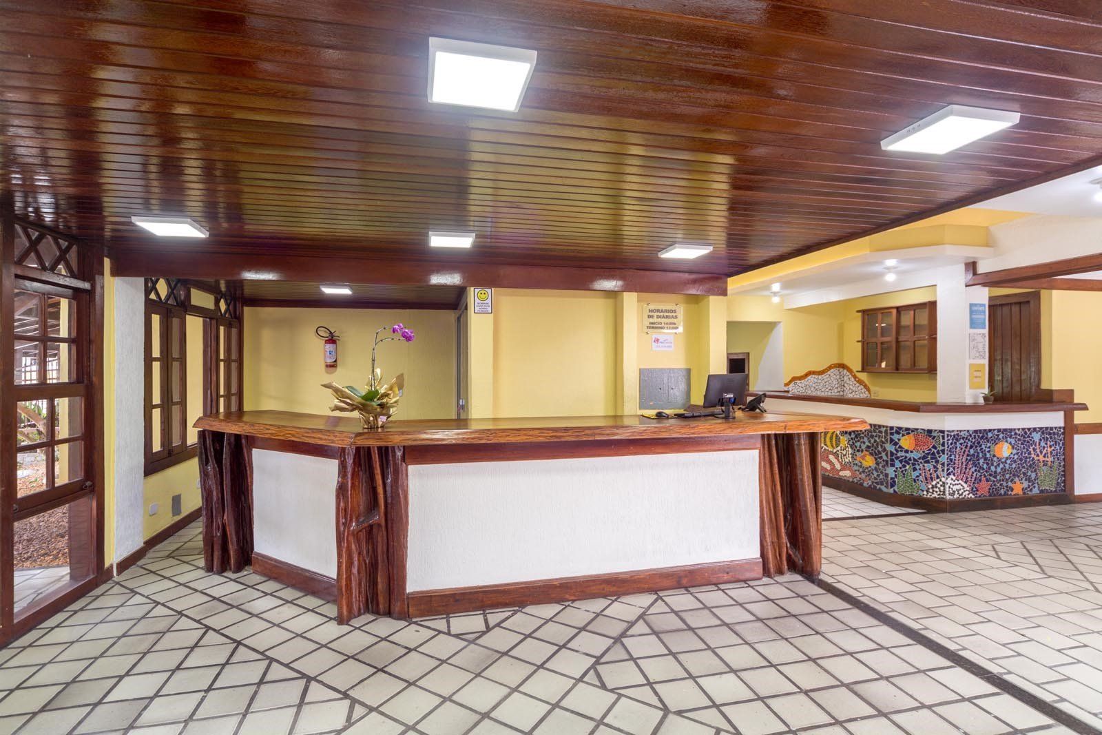 Lobby de hotel com balcão de madeira e piso frio.