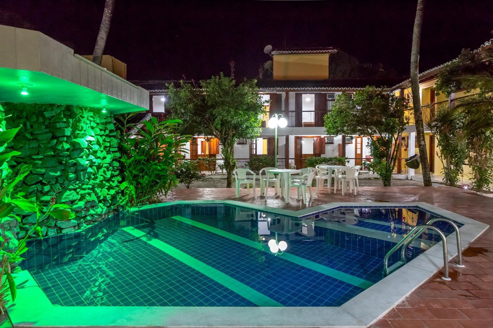 Uma grande piscina é cercada por edifícios e árvores à noite.