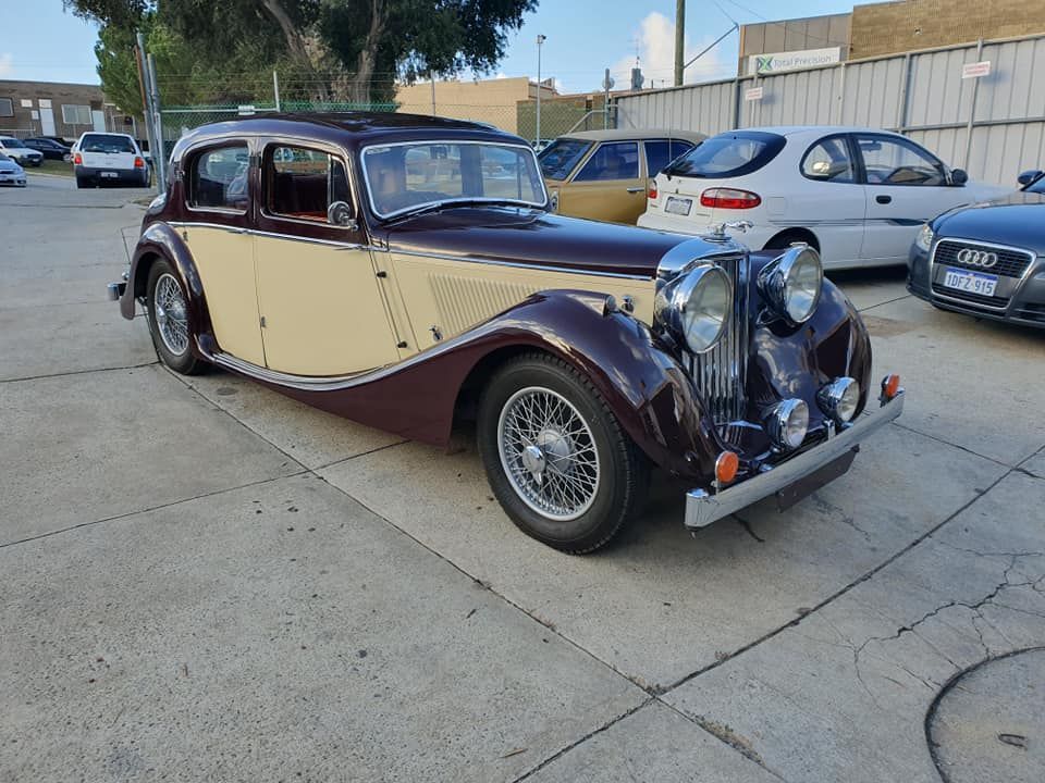 Vintage two-tone maroon and cream Jaguar sedan parked on concrete.
