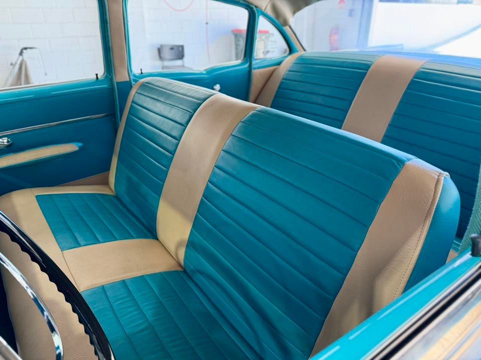 Blue and tan car interior; bench seats with vertical stitching, chrome door handle, light blue panels.