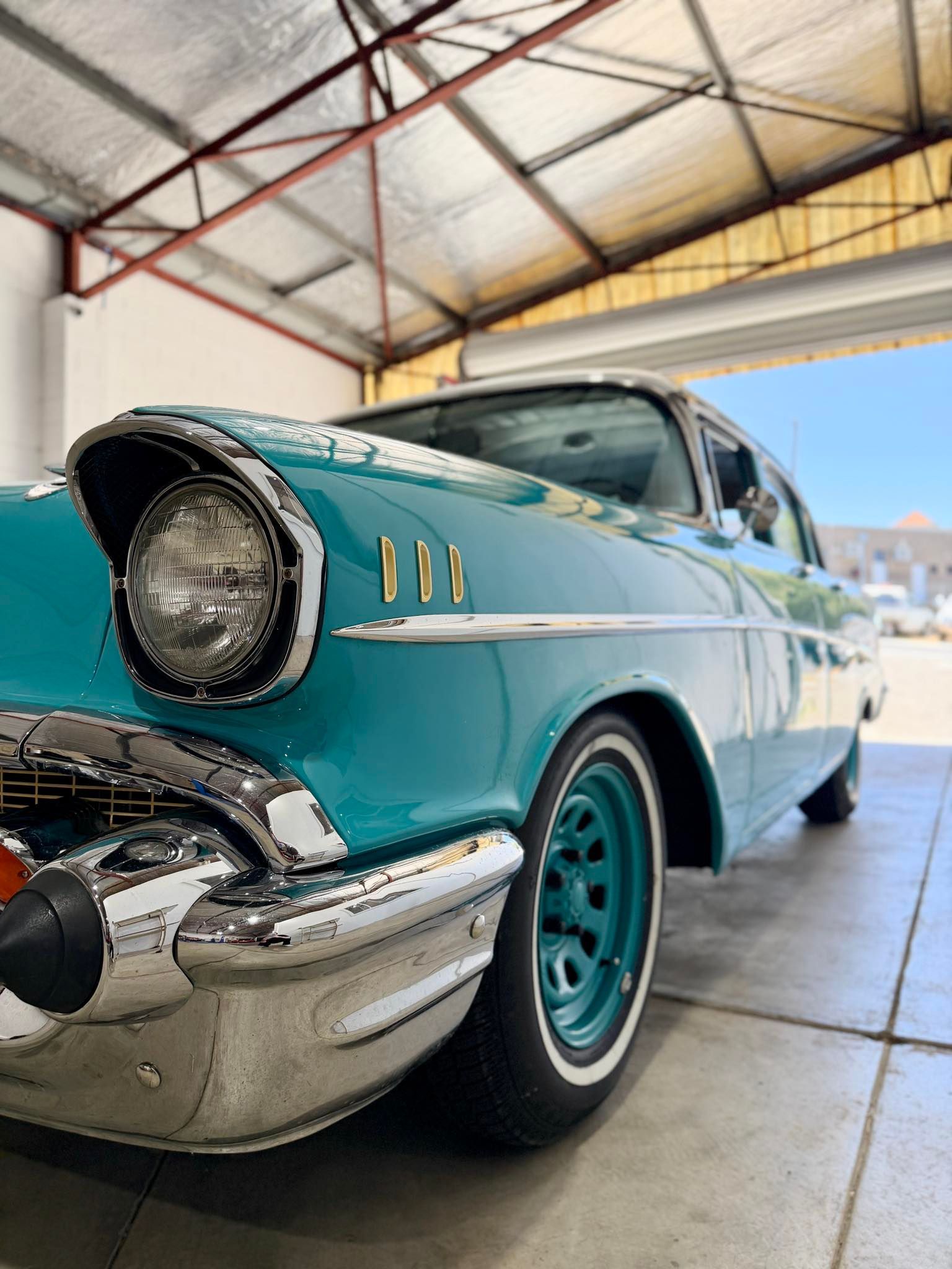 Teal classic car parked inside a garage. White-walled tires, chrome accents.