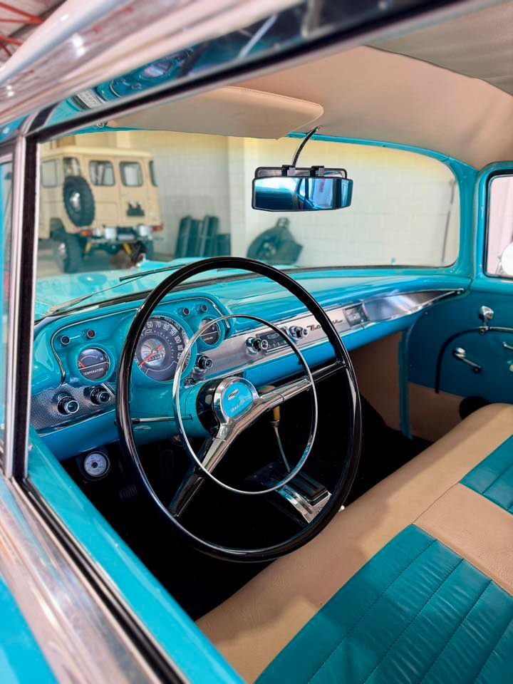 Interior view of a classic turquoise car with black steering wheel and tan seats.