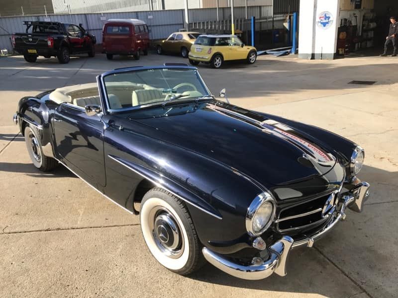 Dark blue vintage convertible with white interior and whitewall tires parked outside.