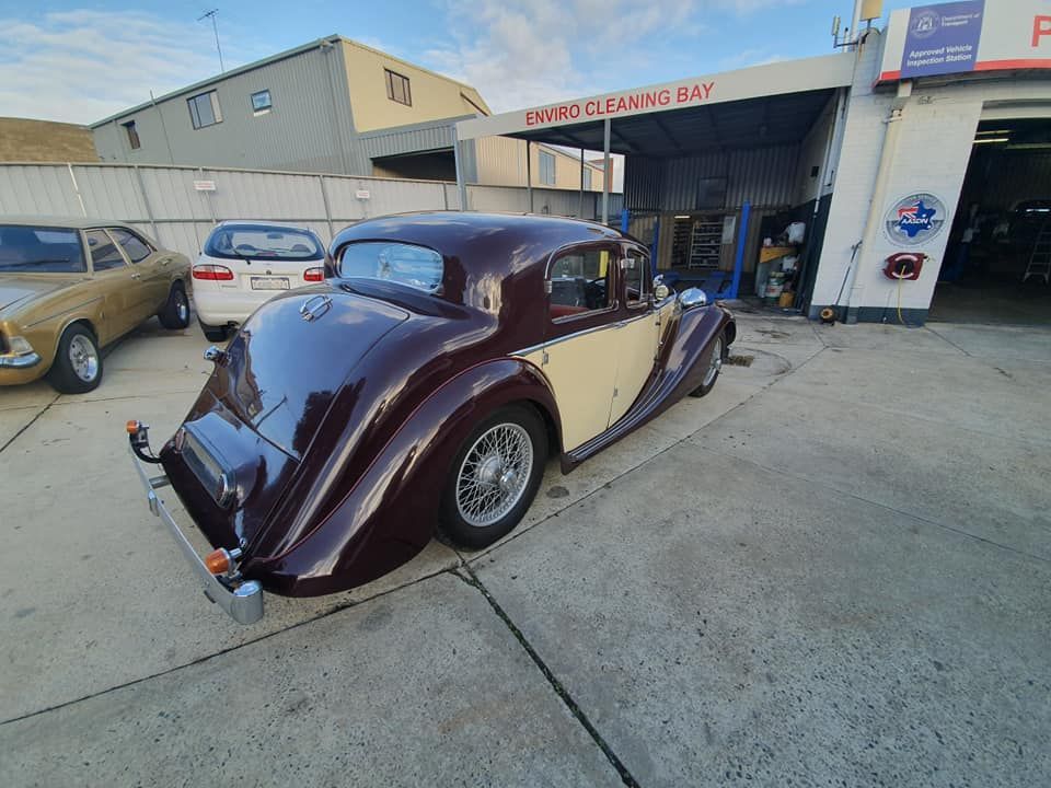 Burgundy and cream vintage car parked in front of a garage.