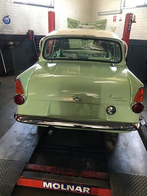 Green vintage car on a lift in a garage, rear view.
