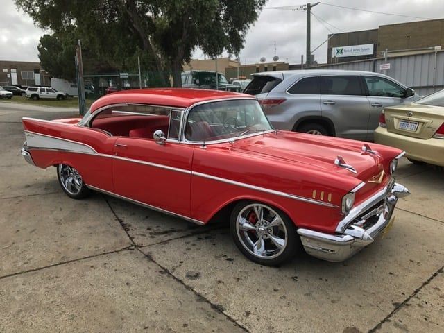 Red classic 1957 Chevrolet Bel Air coupe with chrome accents, parked on concrete.