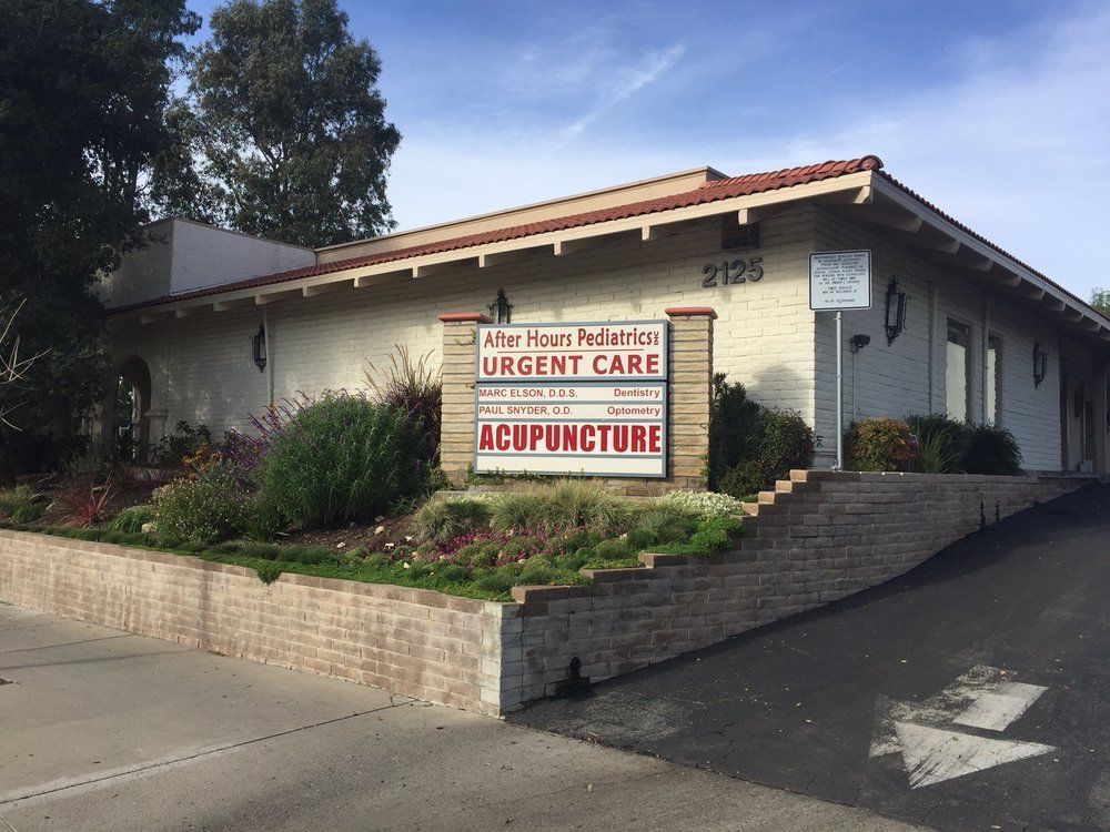 Exterior of a medical office building; sign says Urgent Care and Acupuncture. Brick and stucco building on a slight hill.
