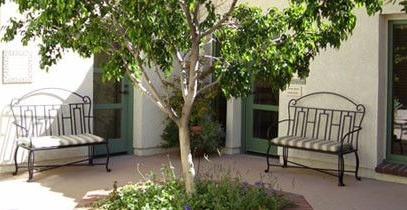 Two wrought iron benches face each other in a courtyard with a tree.