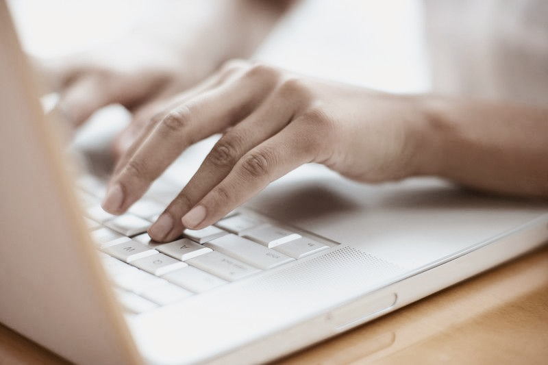 Hands typing on a silver laptop keyboard, close-up shot.