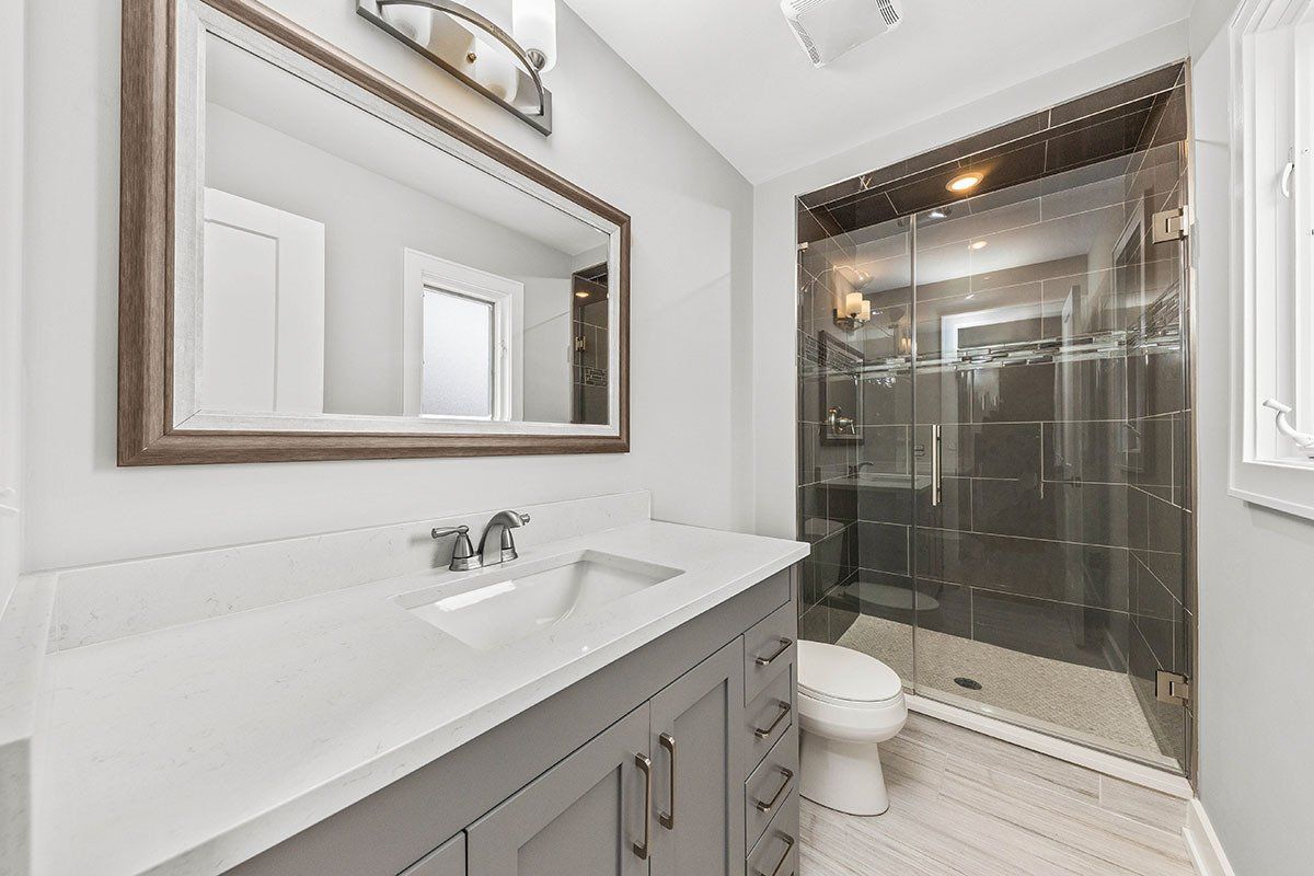 A bathroom with a sink , toilet , mirror and walk in shower.