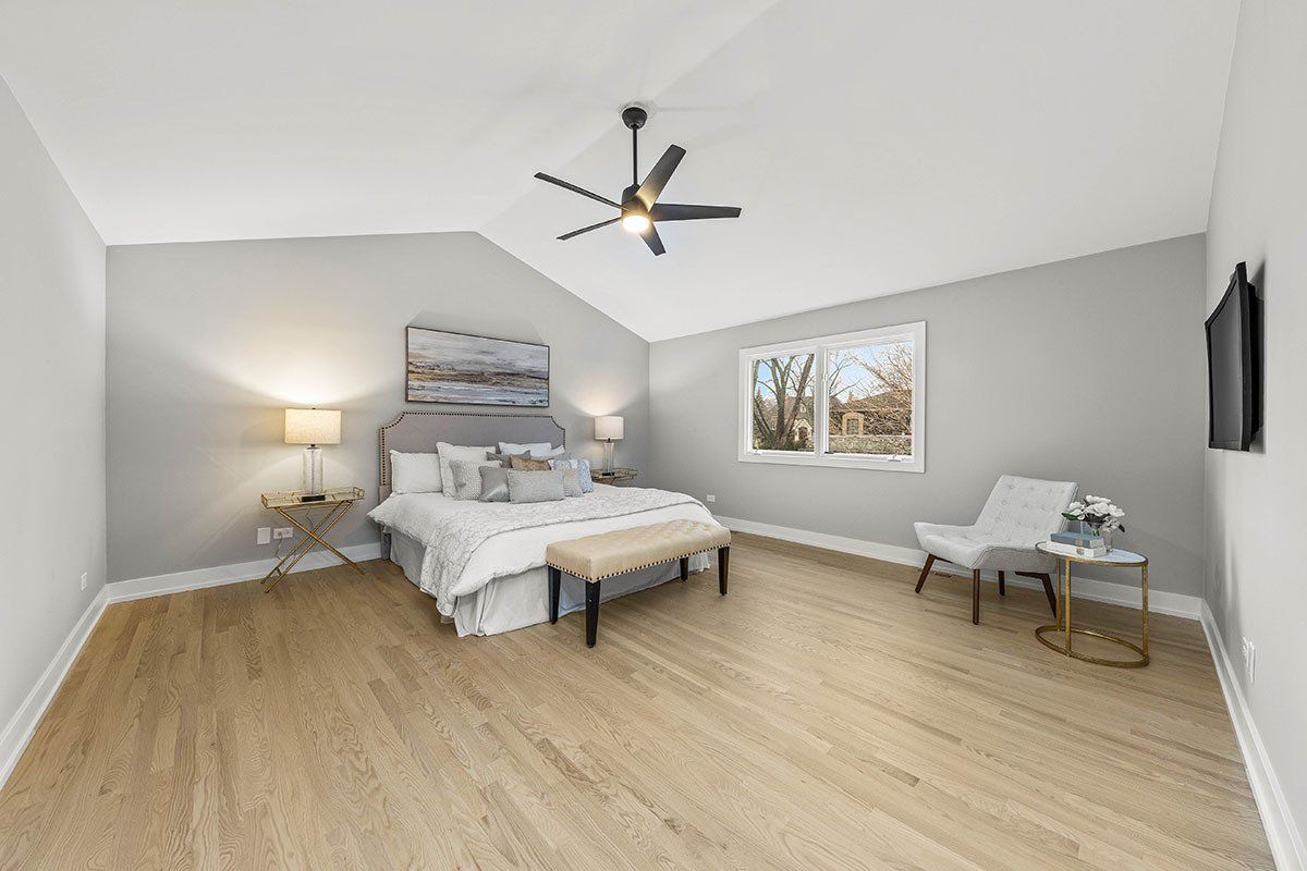 A bedroom with a bed , chair , table and ceiling fan.