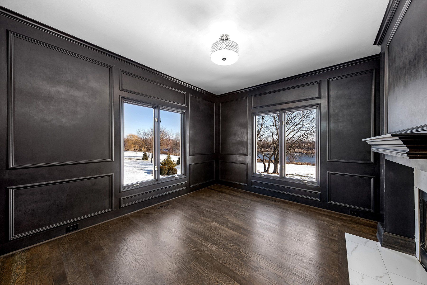 An empty living room with black walls and hardwood floors and a fireplace.