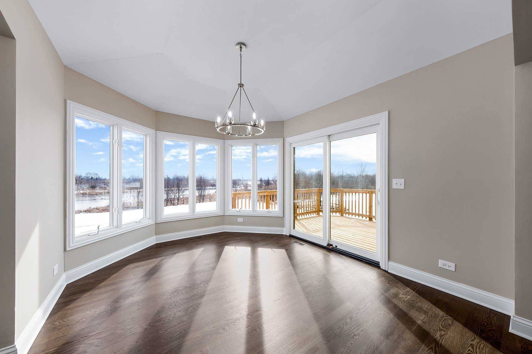 An empty living room with a lot of windows and a chandelier.