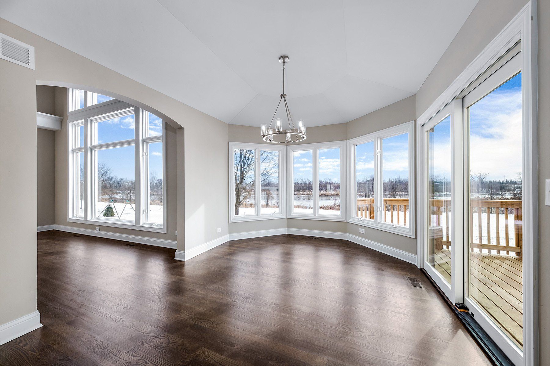 An empty living room with a lot of windows and a chandelier.