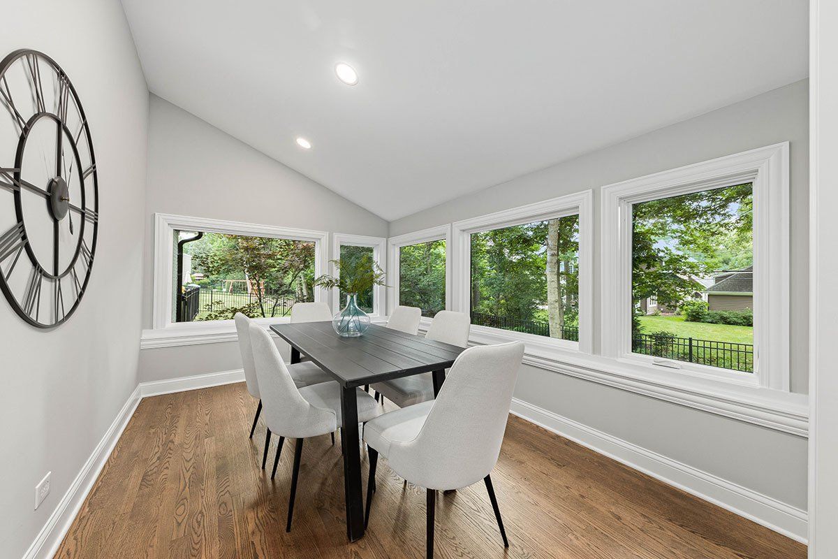 A dining room with a table and chairs and a clock on the wall.