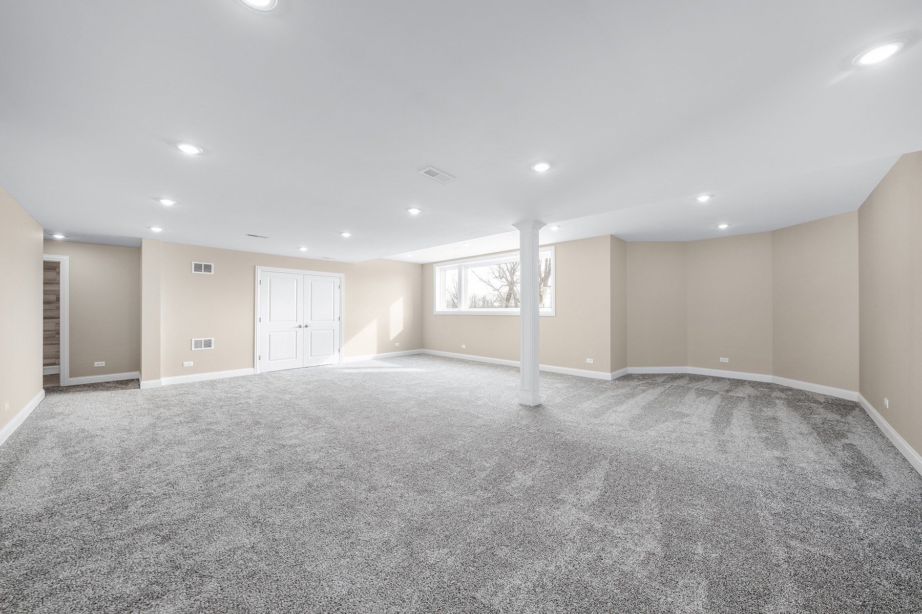 An empty basement with a gray carpet and white walls.