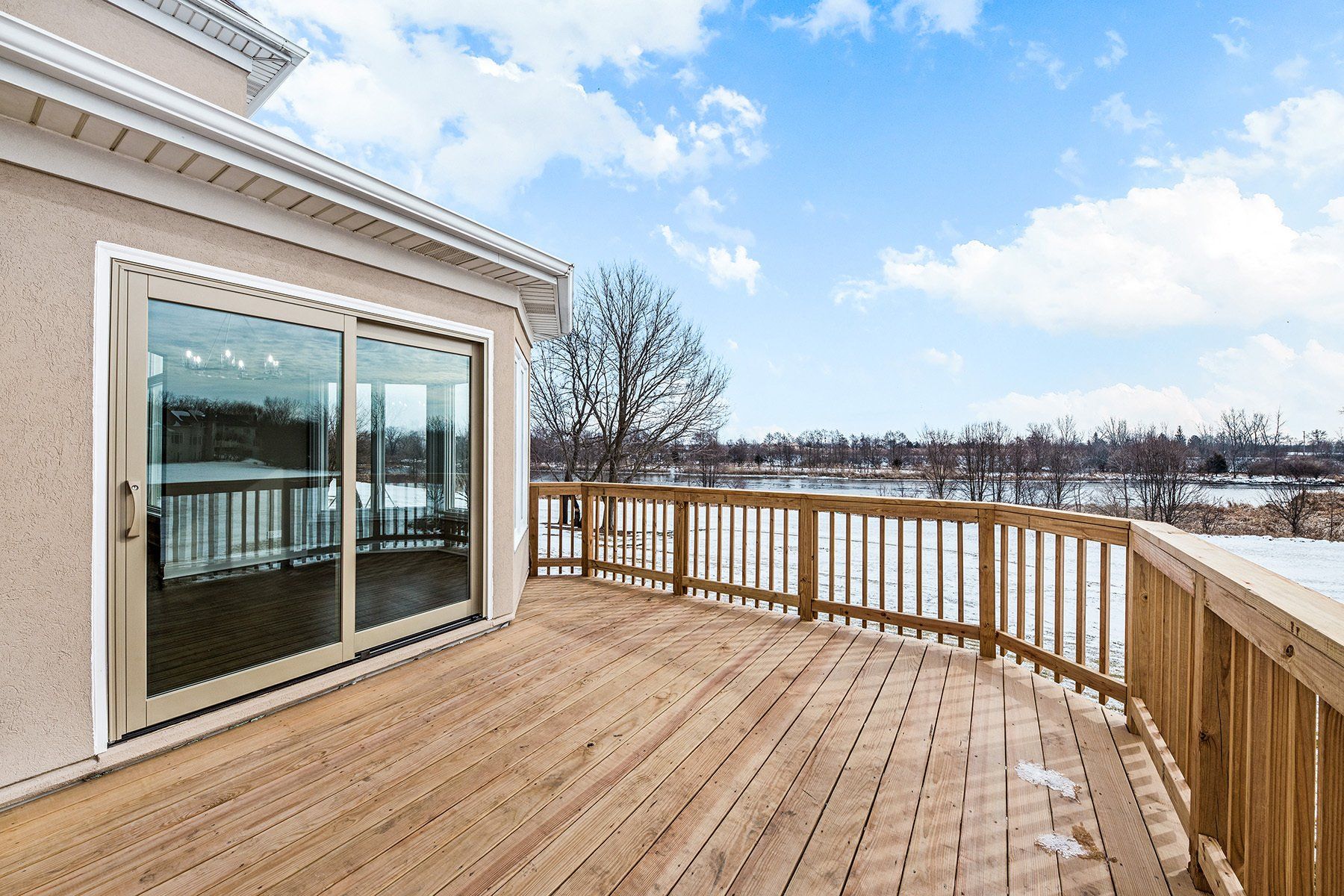 A large wooden deck with a sliding glass door and a view of a lake.