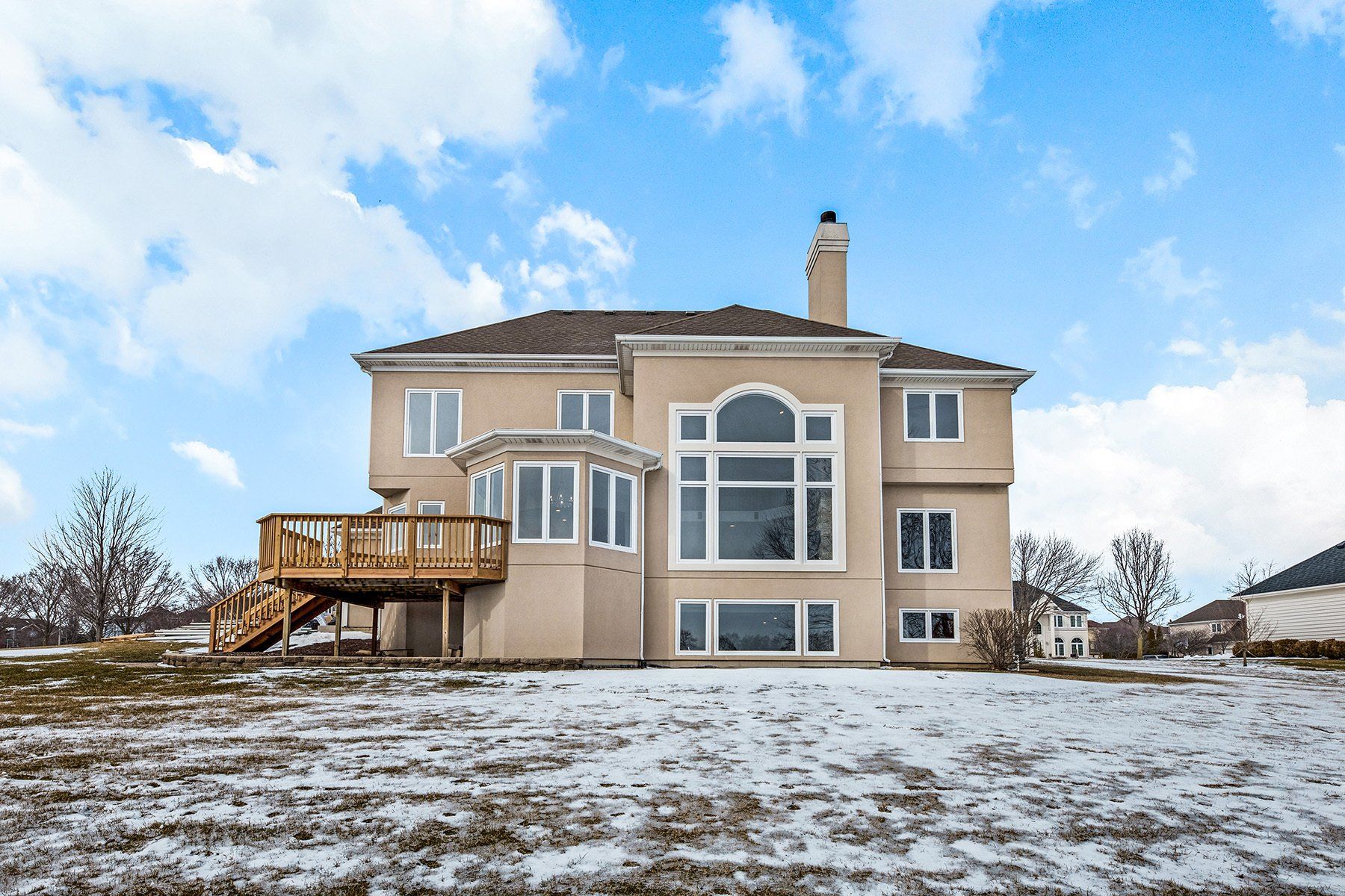 A large house with a large deck is sitting on top of a snow covered field.