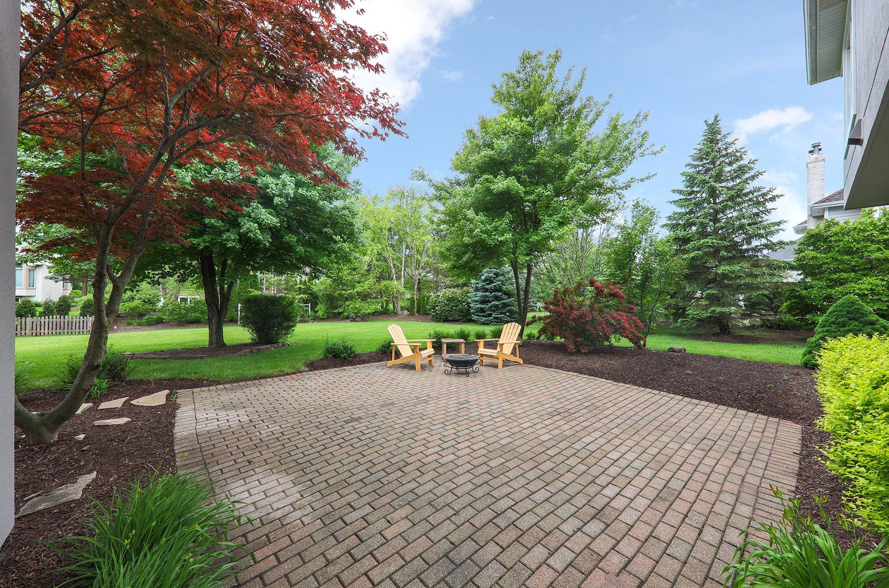A patio with chairs and a fire pit in the middle of a garden.