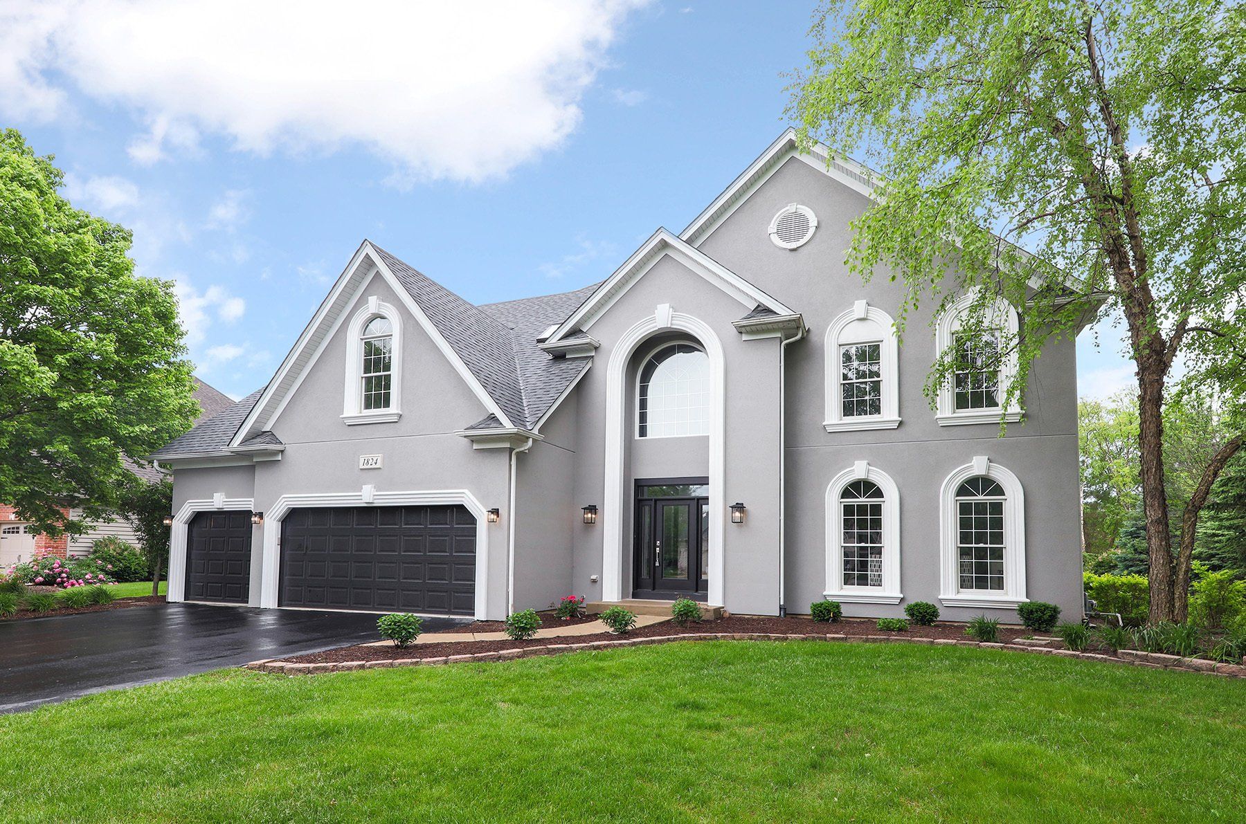 A large gray house with a black garage door is sitting on top of a lush green lawn.