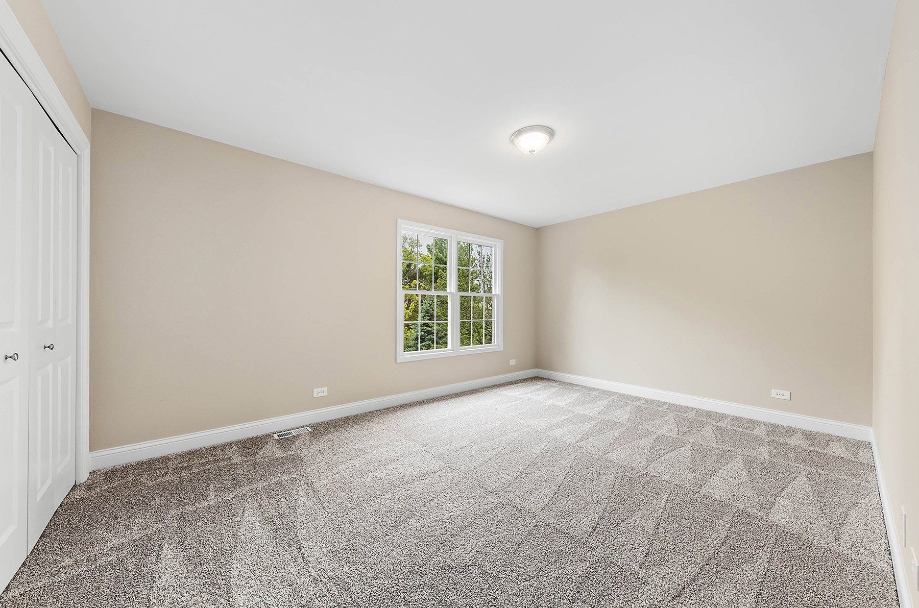 An empty bedroom with a window and a carpeted floor.