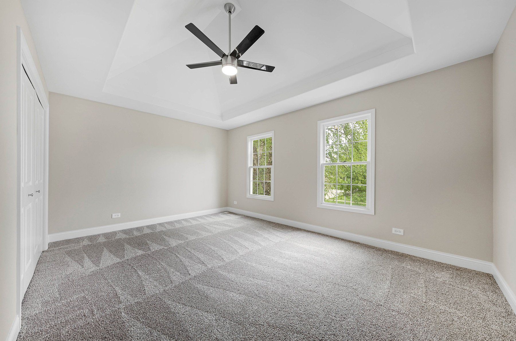 An empty bedroom with a ceiling fan and two windows.