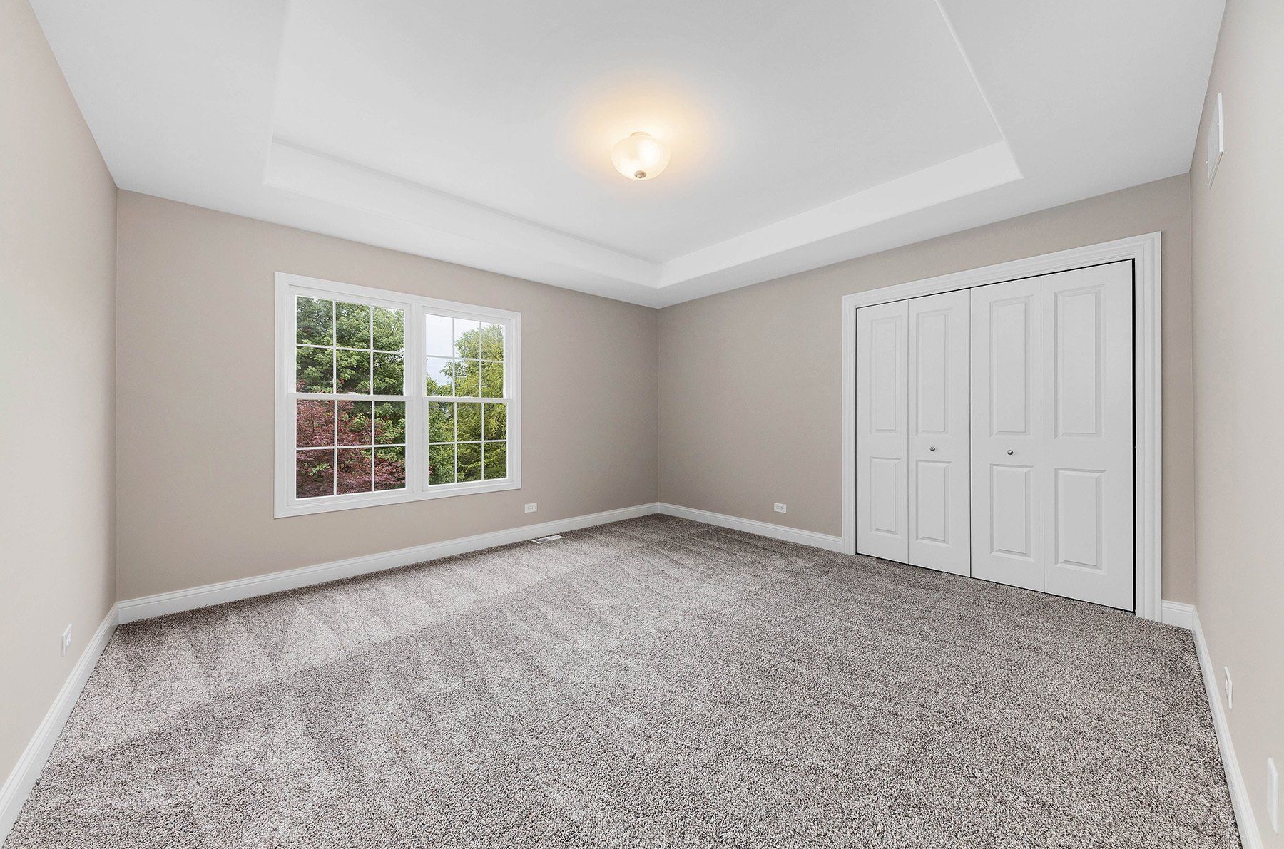 An empty bedroom with a carpeted floor and two windows.